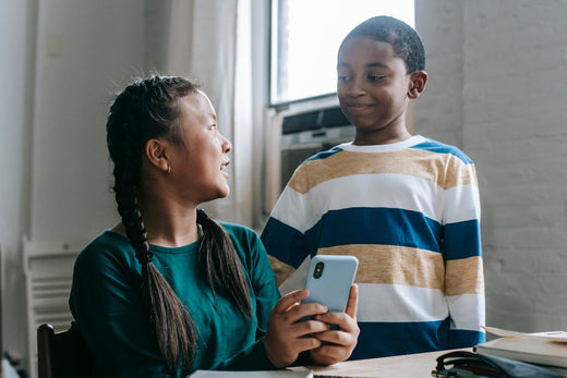 young kids in class talking while using a phone 